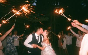 Bride and groom kiss as people whole sparklers above.