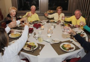 People sitting at a dinner table lifting up their drink glasses and smiling.